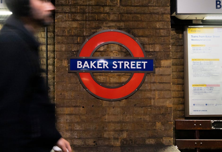 The image depicts the entrance to Hanwell Station, facing a brick building with a large blue sign reading 'Hanwell' at the top. Below the sign, two black and white rectangular signs display 'Hanwell S